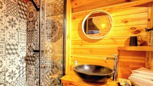 Baño de cabaña de madera con un lavabo grande tipo cuenco, un espejo y baldosas estampadas.