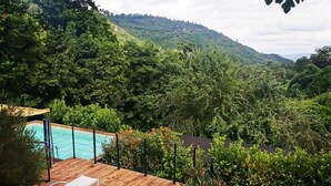 Una terraza de madera con sillones de descanso, una piscina y un paisaje verde exuberante con colinas al fondo.