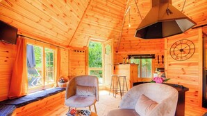 Interior de una cabaña de madera con comedor, barra y un ventanal grande.