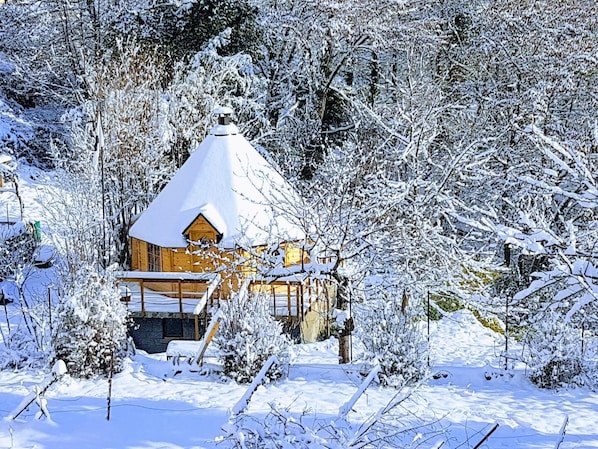 Une cabane en bois, dont le toit est recouvert de neige, entourée d’arbres chargés de neige.