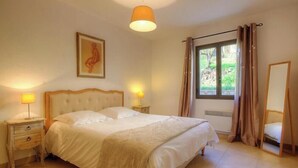 A bedroom with a large bed, bedside lamps, a window with curtains, a framed picture on the wall, and a mirror. - Casale Olmia - Alticeli (MONCALE)