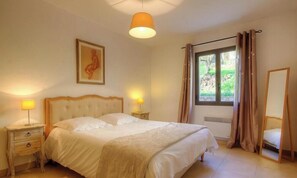 Ein Schlafzimmer mit einem großen Bett, Nachttischlampen, einem Fenster mit Vorhängen, einem gerahmten Bild an der Wand und einem Spiegel.