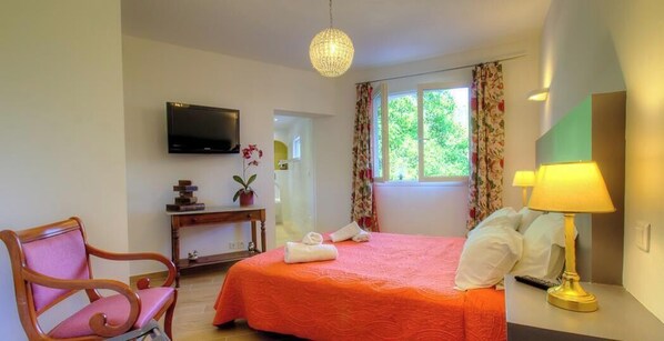 Quarto de hotel com cama, escrivaninha, cadeira, televisão e janela com cortinas.