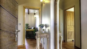 Un pasillo con una puerta de madera, una mesa pequeña con un florero y un accesorio de iluminación.