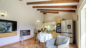Una cocina con vigas de madera, un televisor, una chimenea y un comedor con mesa y sillas.