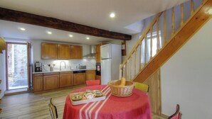 Una cocina con armarios de madera, una mesa de comedor con mantel rojo y una escalera.