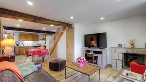 Amplia sala de estar con una escalera de madera, una mesa de comedor, un sofá, un televisor y una chimenea.
