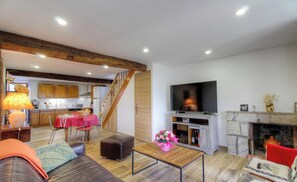 Een ruime woonkamer met een houten trap, een eettafel, een bank, een televisie en een open haard.