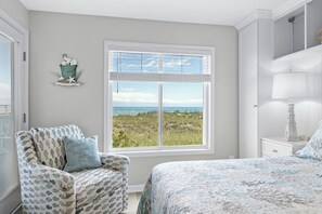 A bedroom with a large window, a chair, a bed, and a nightstand. - Coastal Elegance | Renovated 4BR Oceanfront-Pool & Beach Access (North Myrtle Beach)