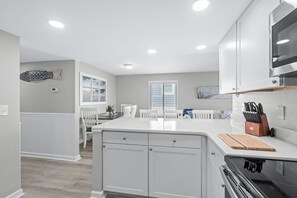 A modern kitchen with white cabinetry, a central island, and a stainless steel range hood. - Coastal Elegance | Renovated 4BR Oceanfront-Pool & Beach Access (North Myrtle Beach)