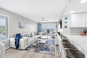 A modern living room with a sofa, coffee table, and a view to the outside. - Coastal Elegance | Renovated 4BR Oceanfront-Pool & Beach Access (North Myrtle Beach)