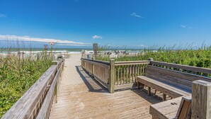 Une promenade en bois menant à une plage, avec un banc et un panneau indicateur.