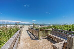 A wooden boardwalk leading to a beach with a bench and a signpost. - Coastal Elegance | Renovated 4BR Oceanfront-Pool & Beach Access (North Myrtle Beach)