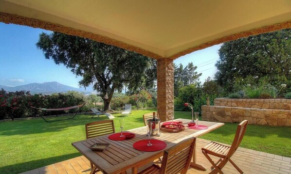 Eine Terrassensitzgruppe im Freien mit Tisch, umgeben von Grünpflanzen und Blick auf Berge.