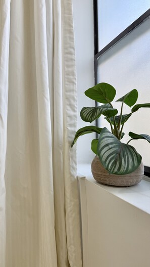 Een raam met witte gordijnen, een potplant met gestreepte bladeren en een stenen pot.