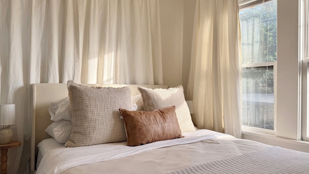 Un dormitorio con cama, cortinas blancas y una ventana.
