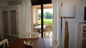 Comedor con una mesa, sillas y una lámpara. Hay una puerta abierta que da a un patio exterior con mesa y sillas.