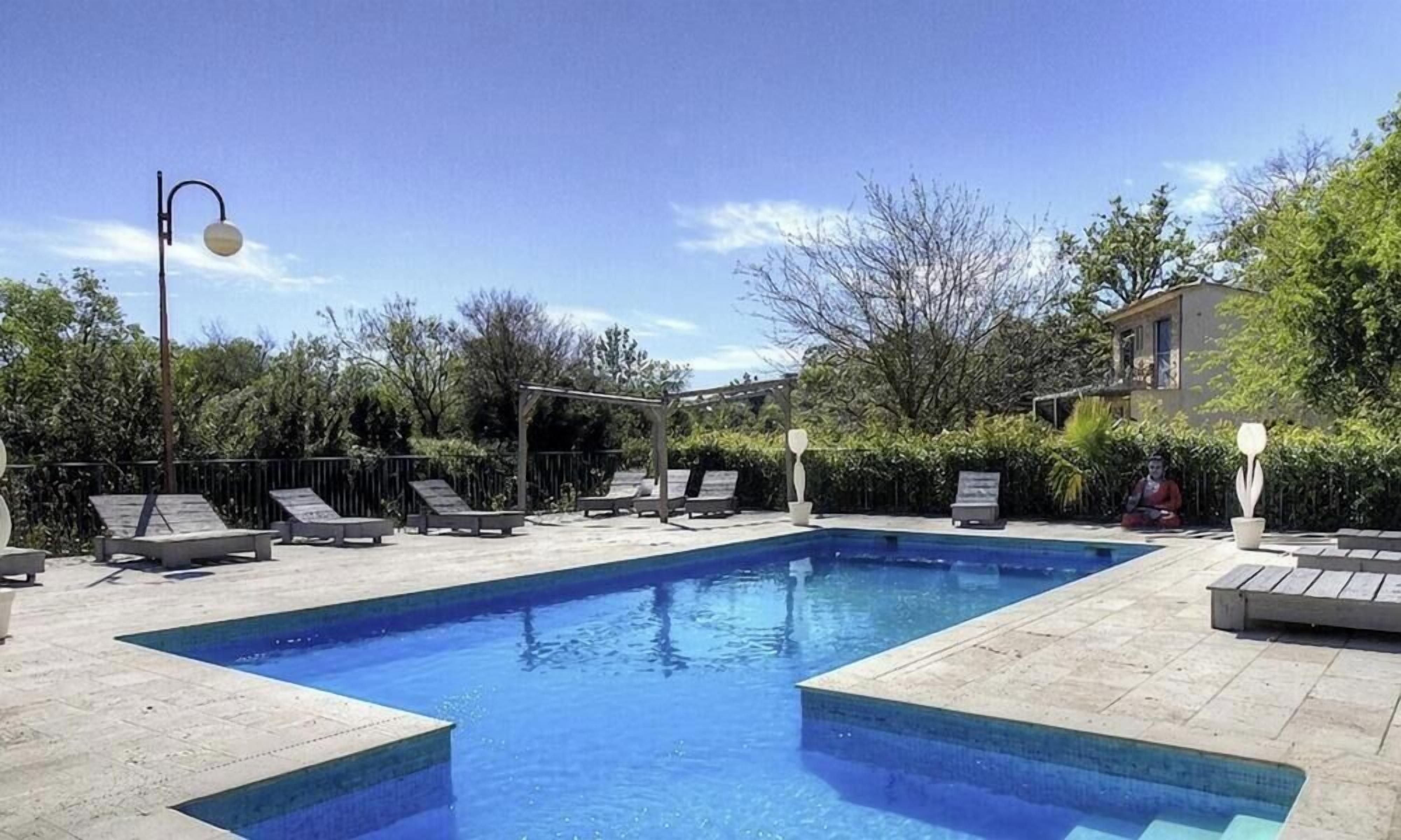 Una piscina rectangular con solárium empinado, rodeada de sillas de descanso y una pérgola.