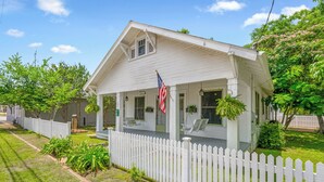 Ein weißes Einfamilienhaus mit Veranda, einer amerikanischen Flagge und einem weißen Gartenzaun.