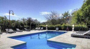 Ein rechteckiger Swimmingpool mit einer gefliesten Liegefläche, umgeben von Liegestühlen und einer Pergola.