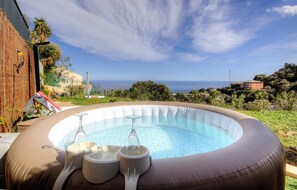Ein Whirlpool mit freiem Blick auf das Meer, umgeben von Grünpflanzen und einer Backsteinmauer.