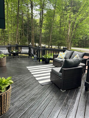 Eine Holzterrasse mit Gartenmöbeln, darunter eine Sitzecke mit Sofa und Stühlen, umgeben von Bäumen.