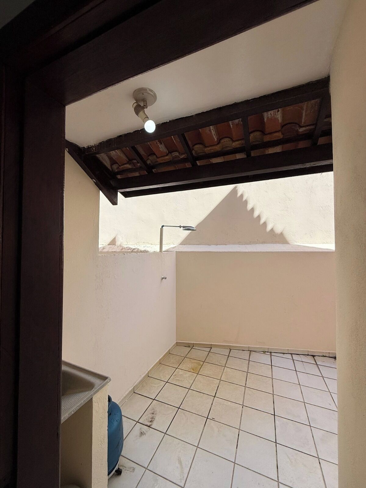 A small, enclosed balcony with a tiled floor, a metal railing, and a ceiling light fixture.