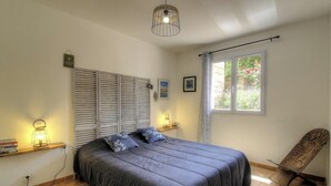 Ett sovrum med en säng, ett fönster med gardiner, en stol och en hylla med böcker och en lampa.