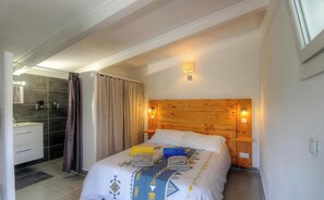 Ein Schlafzimmer mit hölzernem Kopfteil, einem Bett mit gemusterten Betttextilien, einem Nachttisch und einem Badezimmer mit Duschvorhang.