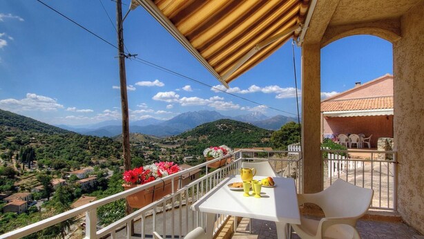 Un balcón con una mesa, sillas y vistas a un paisaje montañoso.