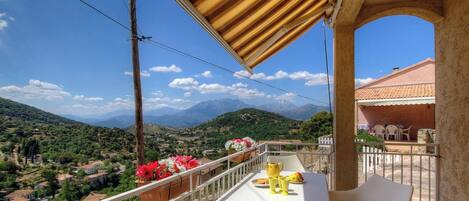 A balcony with a table, chairs, and a view of a mountainous landscape.