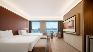 A hotel room with a large bed, a seating area, a TV, and a view of the city. - Crystal Hotel Weihai Happiness Gate (Weihai)
