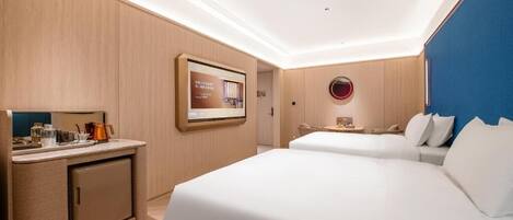 A hotel room with a bed, a desk with a computer, a small kitchenette, and a TV mounted on the wall.