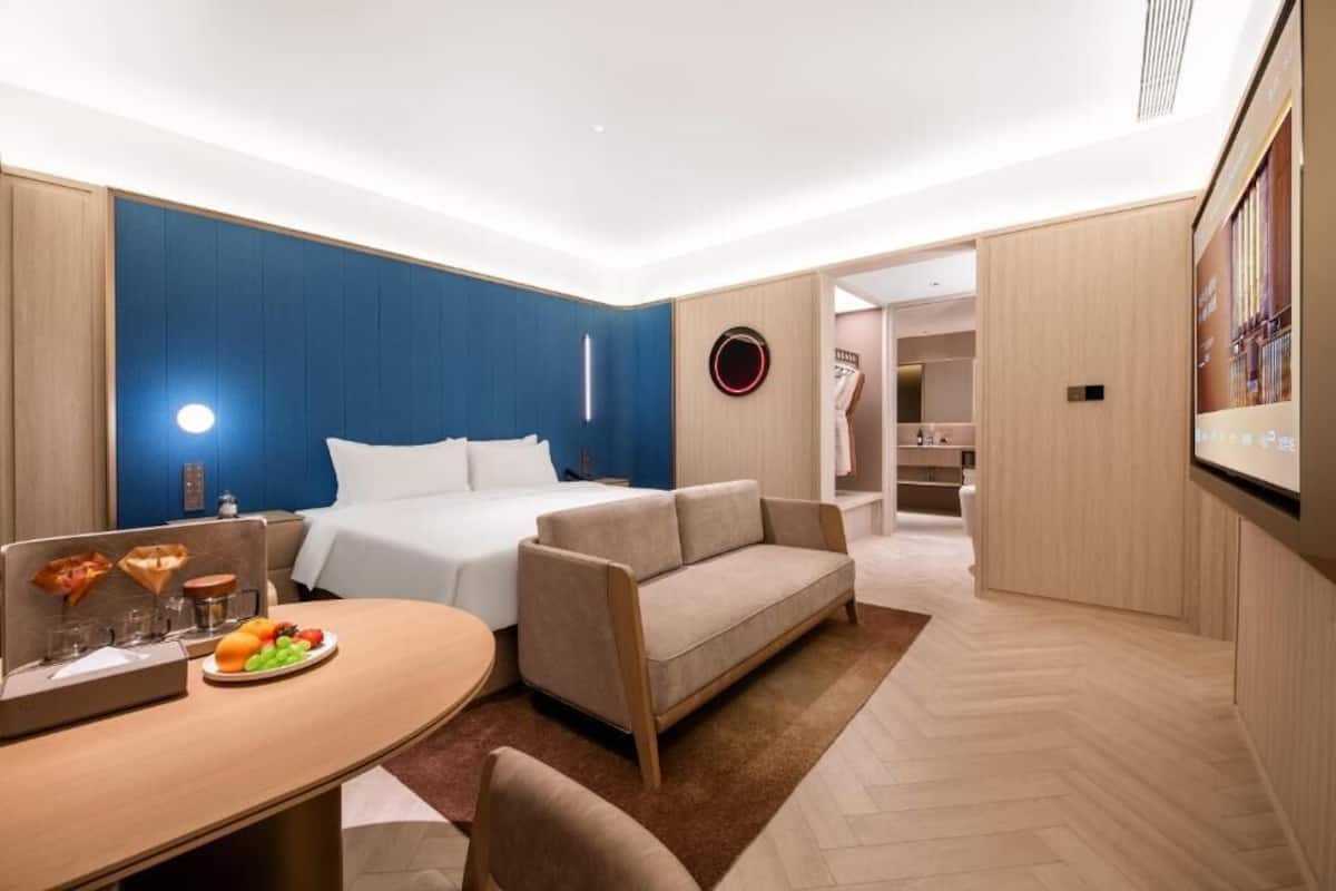 Moderni hotellihuone, jossa on sänky, sohva, ruokailutila pöytineen ja tuoleineen sekä pieni keittiö.