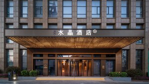 A hotel entrance with a modern facade, a covered entrance area, and a digital display. - Crystal Hotel Weihai Happiness Gate (Weihai)