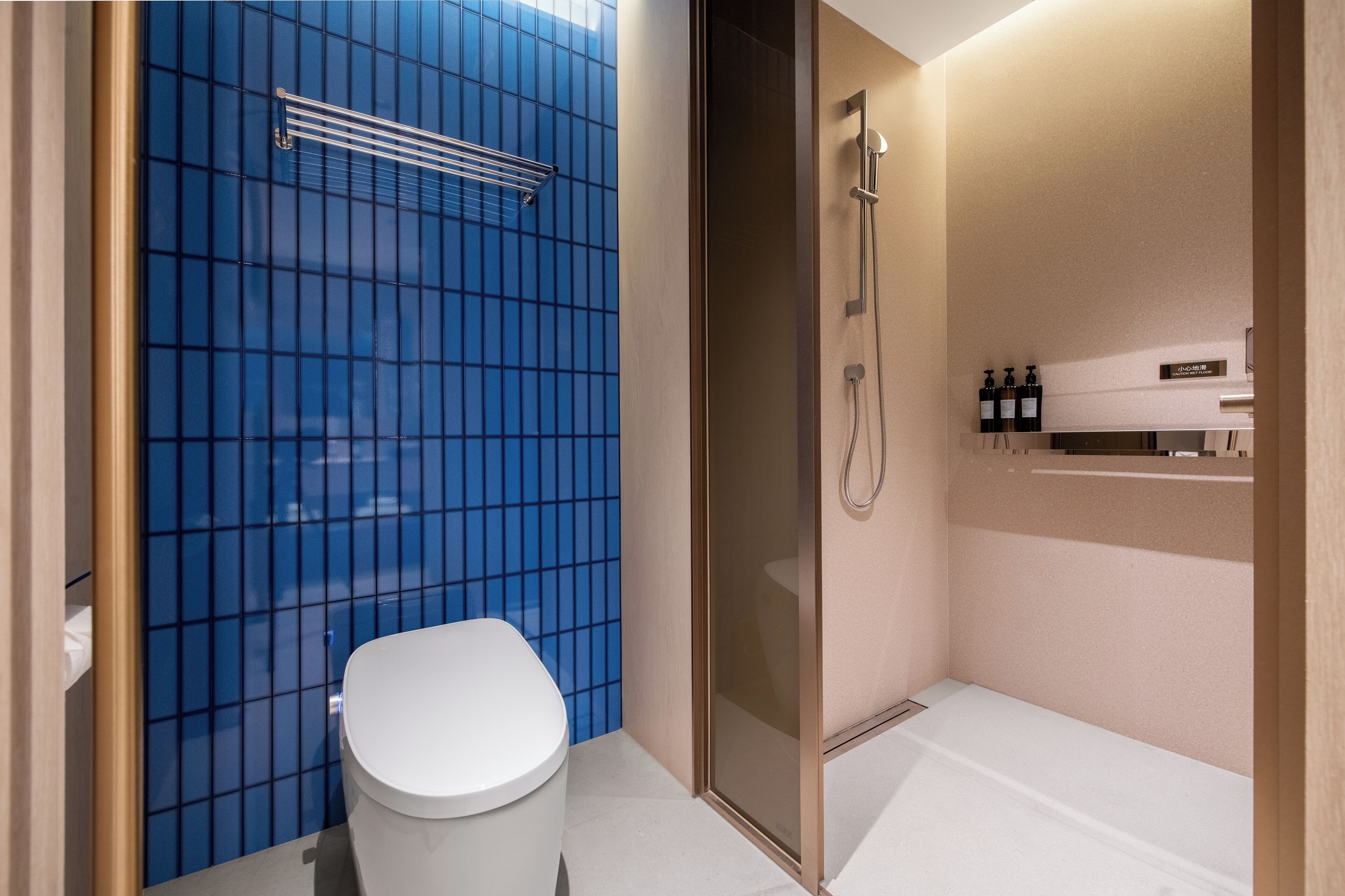 A modern bathroom with a blue-tiled shower enclosure, a white toilet, and a glass shower door.