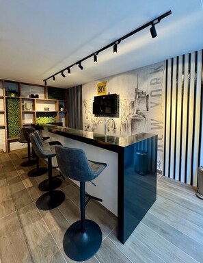 Eine moderne Küche mit Barbereich, Barhocker, einem an der Wand befestigten Fernseher und einem Stadtbild-Wandgemälde.