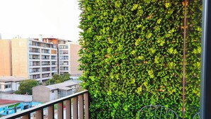 Un balcón con un muro verde, una mesa con dos copas de vino y una botella, y una barandilla.