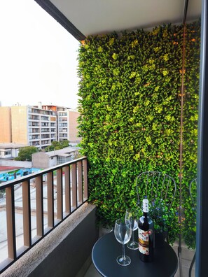 Ein Balkon mit einer grünen Wand, einem Tisch mit zwei Weingläsern und einer Flasche sowie einem Geländer.