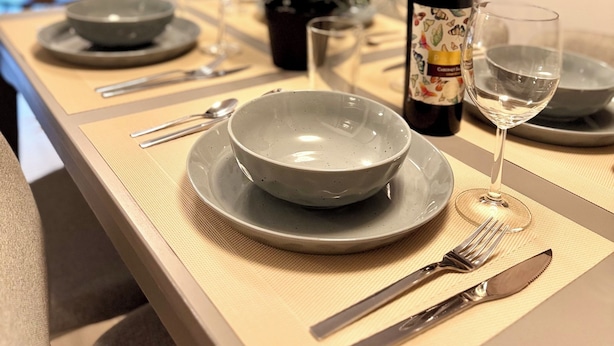 Una mesa de comedor dispuesta con platos, cubiertos, una botella de vino y copas.