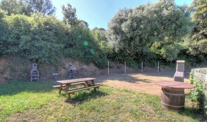 Zona de pícnic amb taula de fusta i bancs, envoltada d'arbres i una tanca.