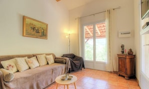 Ein Wohnzimmer mit einer Couch, einem kleinen Tisch mit Schalen, einem Bild an der Wand und einem Fenster mit Vorhängen.
