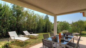 Eine Terrassensitzgelegenheit mit Esstisch, umgeben von Stühlen, und ein überdachter Bereich mit Blick auf einen üppigen Garten.