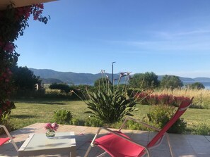 A patio with a table and chairs, a vase with a flower, and a view of a lake and mountains.
