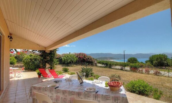 An outdoor dining area with a table set for two, overlooking a scenic landscape with mountains and a body of water.