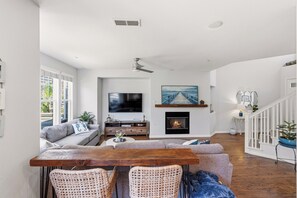 A modern living room with a fireplace, a TV, and a dining area with wicker chairs. - Beachwood Retreat 30-Night Minimum (Carlsbad)