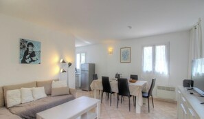 A living room with a sofa, a dining table with chairs, a kitchen area with a refrigerator, and a TV on a stand. - Tivarellu - FIGARI - Gîte (FIGARI)
