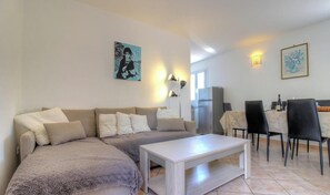 A living room with a sofa, a coffee table, a dining table with chairs, and artwork on the walls. - Tivarellu - FIGARI - Gîte (FIGARI)