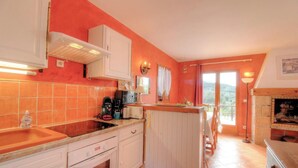 Una cucina con zoccolo di piastrelle rosse, mobili bianchi, forno integrato e vista all'esterno tramite una porta in vetro.