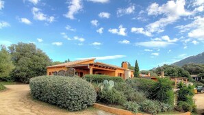 Una casa con tetto in tegole, immersa nel verde e sotto un cielo sereno.